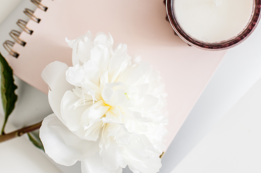 A white peony sits on a notebook and a candle